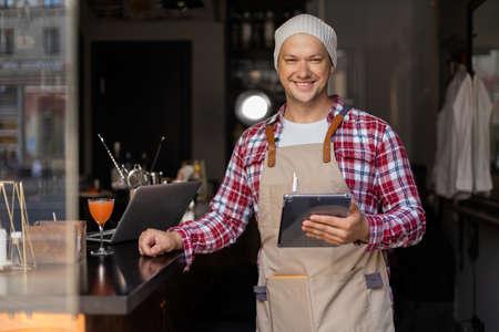 Young male owner using digital tablet while standing in cafe.