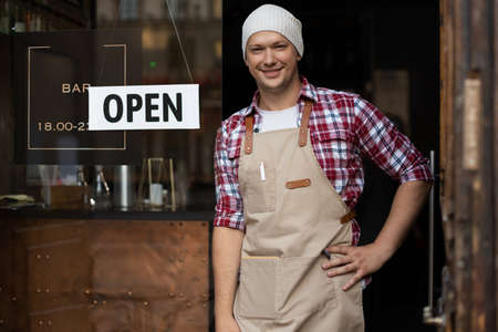 Smiling male owner of bar is standing outdoors. He is inviting everybody to come in. openの写真素材