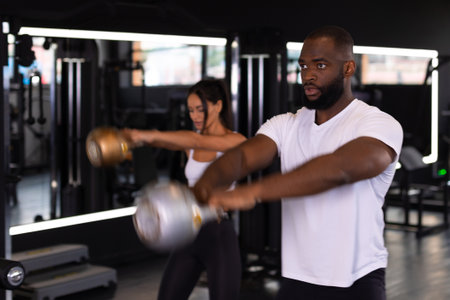 Fit and muscular couple focused on lifting a dumbbell during an exercise class in a gym.の写真素材