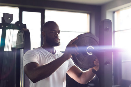 Muscular sporty african man adding weight on barbell at gym