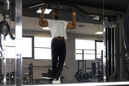 Fit and muscular african man pulling up on horizontal bar in a gym