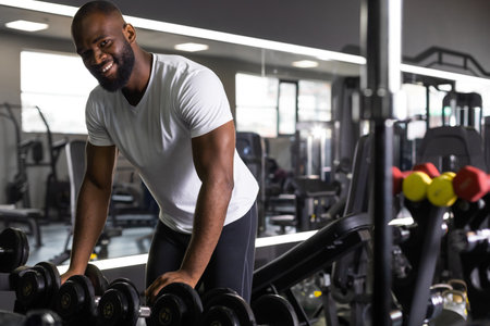 Fitness african man in training showing exercises with dumbbells in gym