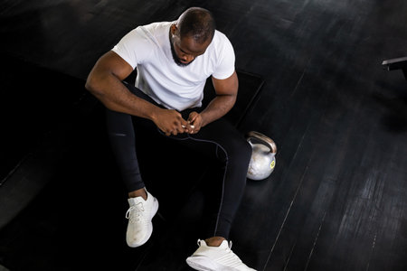 Sporty african man resting, looking at phone having break after doing exercise.の写真素材