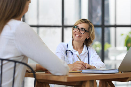 Middle aged female doctor therapist in consultation with patient in officeの写真素材