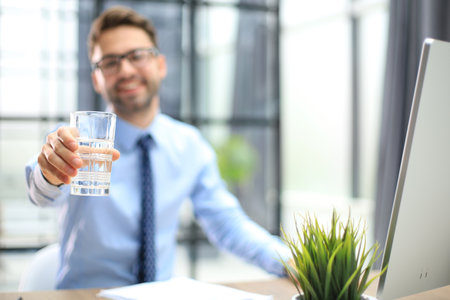 Handsome businessman using PC and drinking water in office area.の写真素材