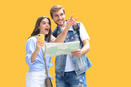 Beautiful young couple holding a map and smiling while standing on yellow background.