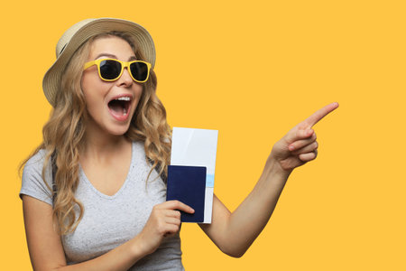 Beautiful blonde woman wearing summer clothes posing with passport with tickets on yellow backgroundの写真素材