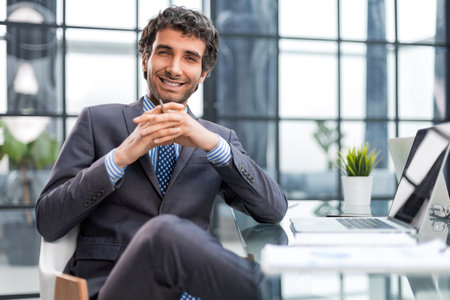 Portrait of young businessman sitting at his desk in the officeの写真素材