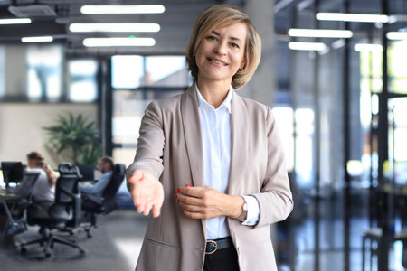 Business woman with an open hand ready for handshake in office.