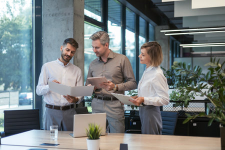 Three business people discussing work together using a tablet and laptop taking notes in a modern officeの写真素材