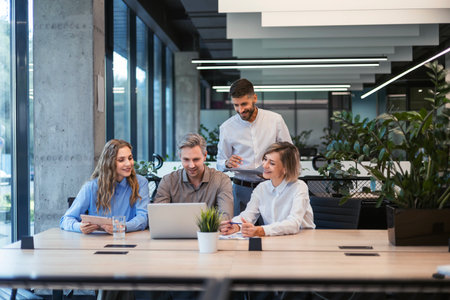 Four business professionals using laptop on desk discussing strategy company.
