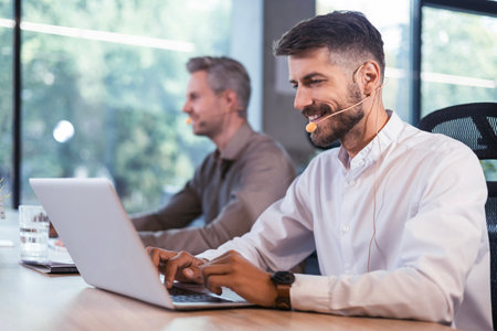 Two call center agents talking with customers while working on laptops at office.の写真素材