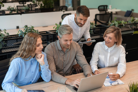 Successful businesspeople working in a coworking space working with laptop discussing strategy and...