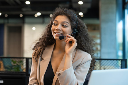 African american positive young woman with headset, sit in modern office, talking with colleagues or having online consultation with clients by video call.の写真素材