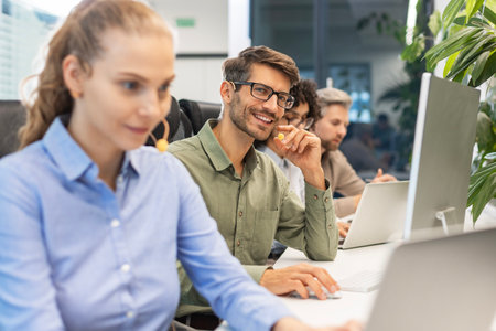 Professional customer support agent man in assisting customers at call center office, with colleagues in the backgroundの写真素材