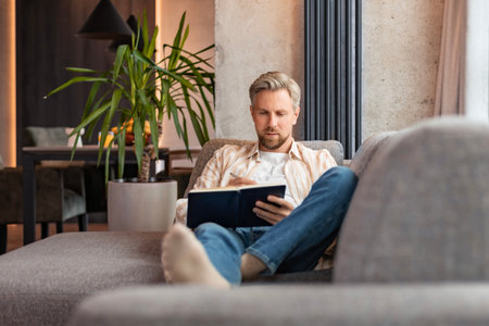 Young businessman sitting on sofa at home and writing notes down on a notepad.の写真素材