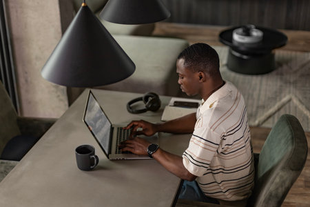 A serious young african entrepreneur accountant, financier, analyst, auditor sits at home at the table. He types on a laptopの写真素材