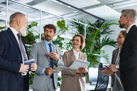 Five business people discussing work together using a tablet in a modern office.の写真素材