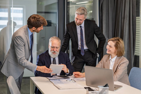 Business people discussing work together using a tablet and laptop taking notes in a modern office.