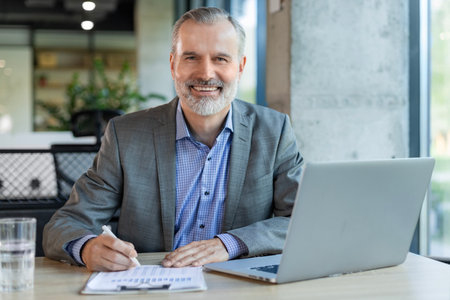 Portrait of adult businessman sitting at his desk in the office and smiling looking at camera.