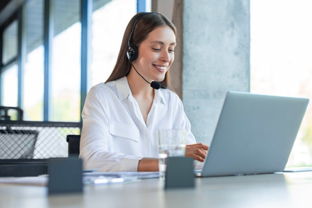 Friendly female helpline operator in call center. Young woman working in call center and holding...