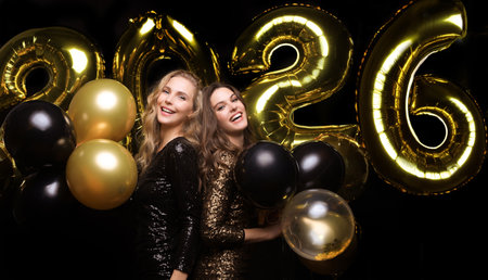 Happy gorgeous girls in stylish party dresses holding gold balloons, having fun at New Year's Eve...