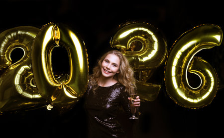 Happy gorgeous girl in stylish party dress holding gold 2026 balloons, having fun at New Year's Eve Partyの写真素材