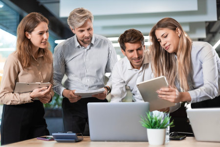 Business people discussing work together using a tablet and laptop taking notes in a modern office.の写真素材