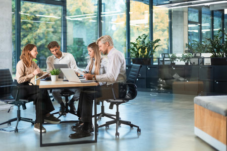A view through a glass partition shows a modern, busy office interior. Business people are working at desk.の写真素材