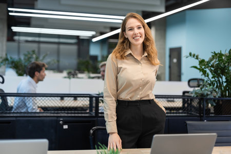 Attractive young businesswoman standing, looking at camera with colleagues on the background.