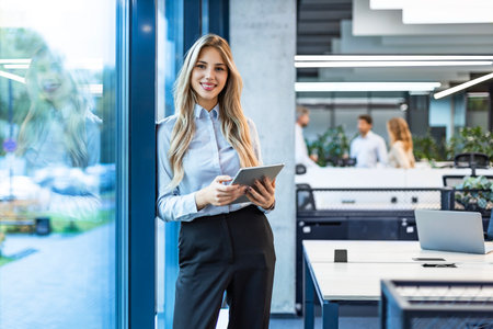 Young elegant business woman standing with digital tablet near office window.
