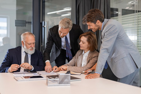 Four business people discussing work together using a tablet in a modern office.