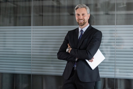 Smiling businessman standing in office with tablet.