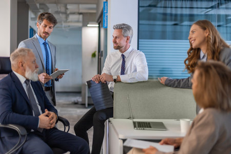 Business people discussing work together using a tablet and laptop taking notes in a modern office.