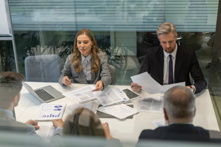 A view through a glass partition shows a modern, busy office interior. Business people are working at desk.の写真素材