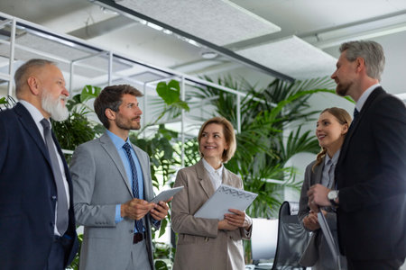 Five business people discussing work together using a tablet in a modern office.