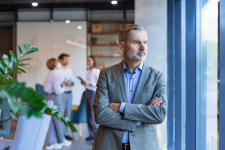 Smiling mature businessman manager executive standing in office with colleagues on the background.