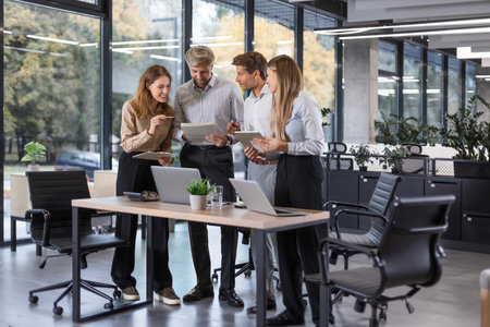 Business people discussing work together using a tablet and laptop taking notes in a modern office.