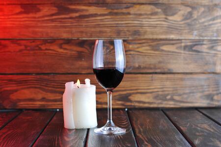 A glass of red wine with a bottle and a candle on a wooden background.の写真素材