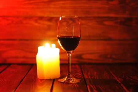 A glass of red wine with a bottle and a candle on a wooden background.の写真素材