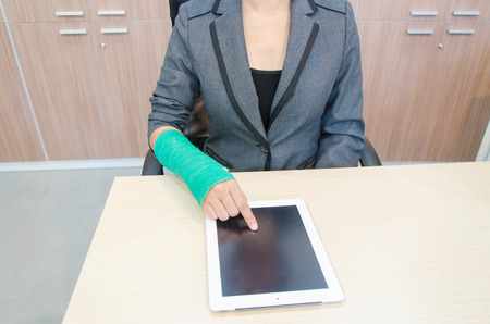 Injured businesswoman with broken hand  and green cast on the wrist using tablet computerの写真素材