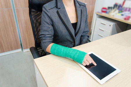 Injured businesswoman with broken hand  and green cast on the wrist using tablet computerの写真素材