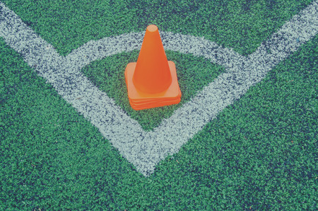 Old artificial green turf texture with white line marks and orange plastic coneの写真素材