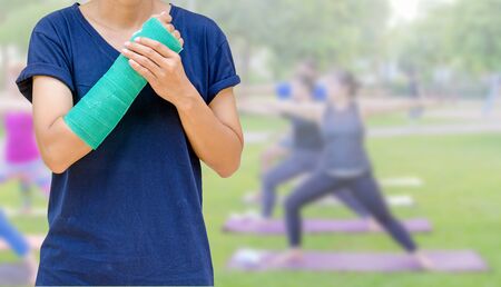 broken arm with green cast on blurred woman fitness group - yoga teamの写真素材