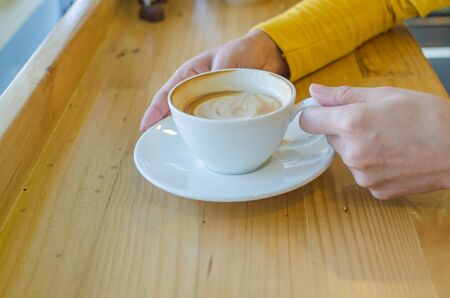 hand holding white coffee cup on wood table in coffee cafe.の写真素材