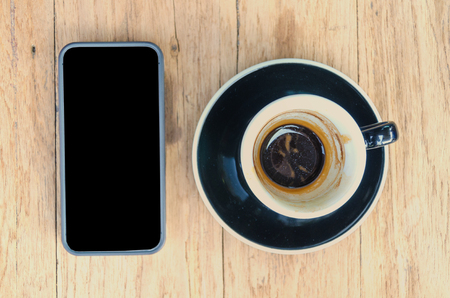 black coffee cup and black smart phone on wood table.の写真素材