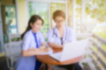 Blurred two female doctor with stethoscope, clipboard and Laptop on desk,Doctor working in clinic writing a prescription,  Health care and medical concept.の写真素材