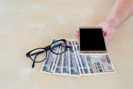 hand woman with Japanese currency yen bank notes , glasses and using smart phone.の写真素材