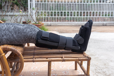 injury woman with black splint on leg  sitting on wooden chair at home, Travel insurance concept.の写真素材