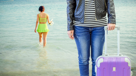 woman tourist wearing jeans and a black leather jacket standing and holding her hand a purple suitcase on view back woman with green bikini at andaman sea background, travel concept.の写真素材